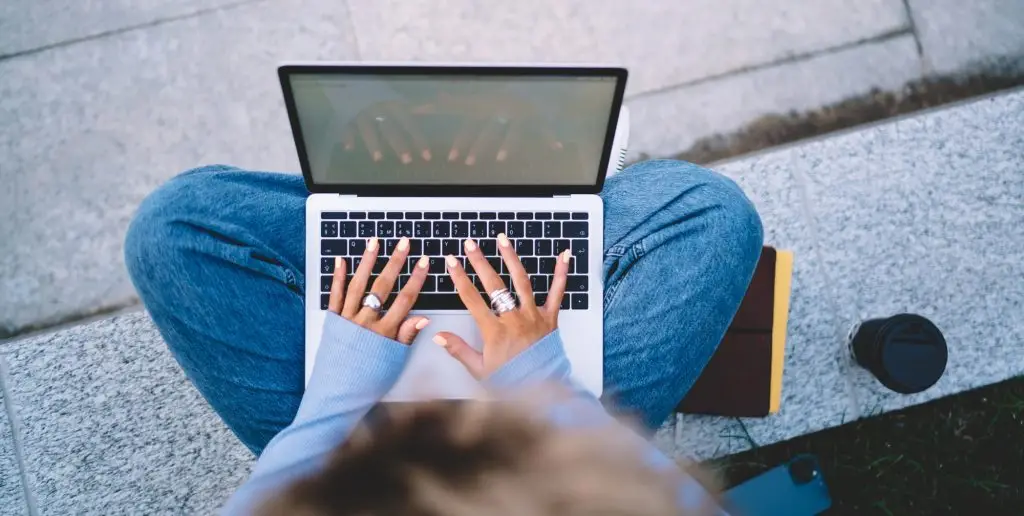 Faceless woman sitting with laptop on knees and typing text